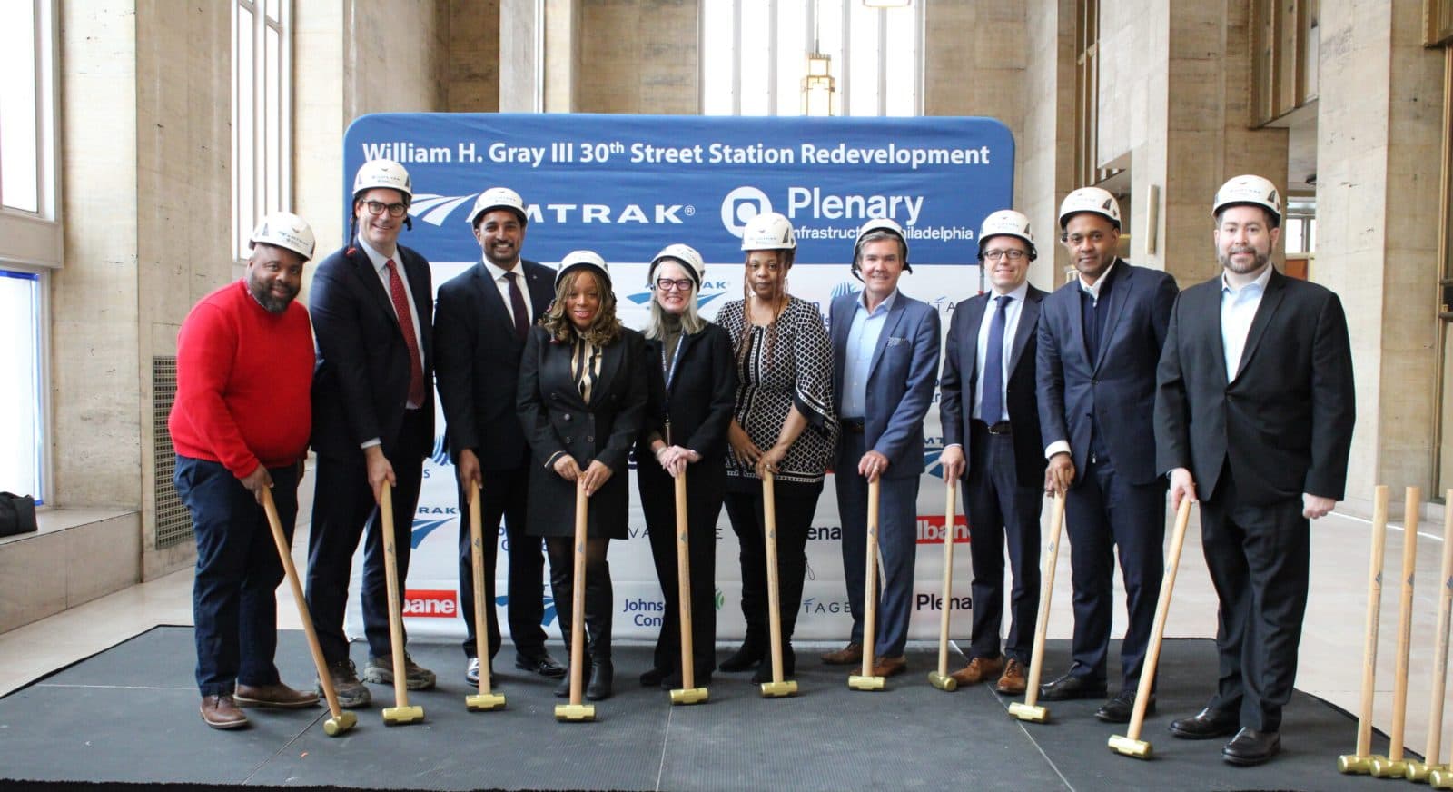 Team photo with representatives holding golden sledgehammers at a construction kickoff event